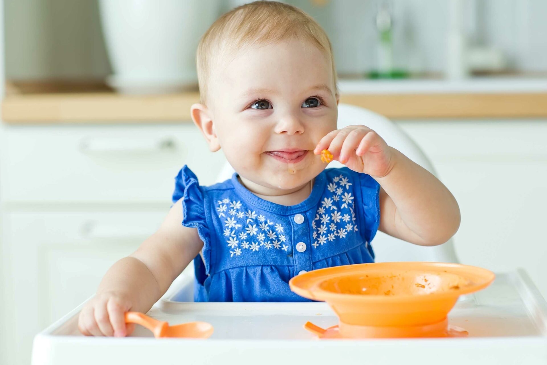 pokarm stały w diecie dziecka, małe dziecko je zupę z pomarańczowej miseczki