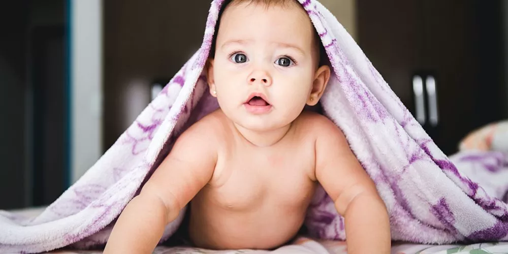 niemowlak podnosi się na rękach, przykryty fioletowym kocem