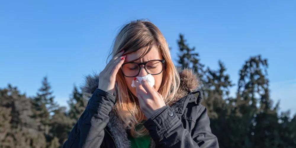 Kobieta na dworze trzyma chusteczkę przy twarzy, alergia na olszę