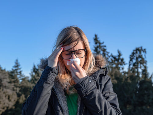 Kobieta na dworze trzyma chusteczkę przy twarzy, alergia na olszę