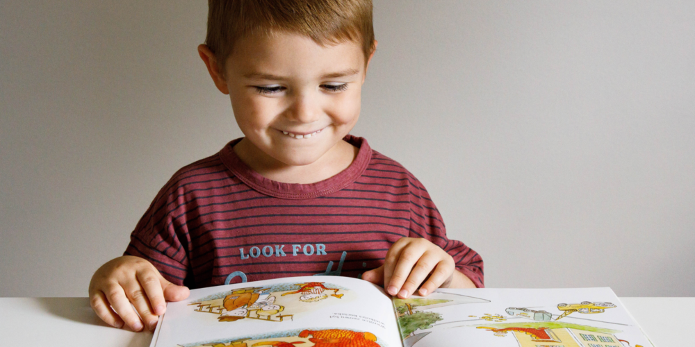 Uśmiechnięty chłopiec ogląda ilustracje w książce dla dzieci