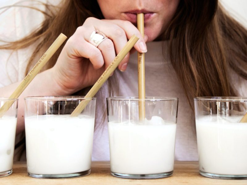 Cztery szklanki mleka ze słomkami, z jednej pije kobieta