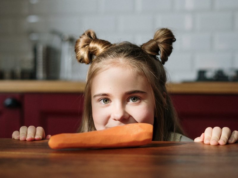 A girl with ponies, a peeled carrot is lying in front of her