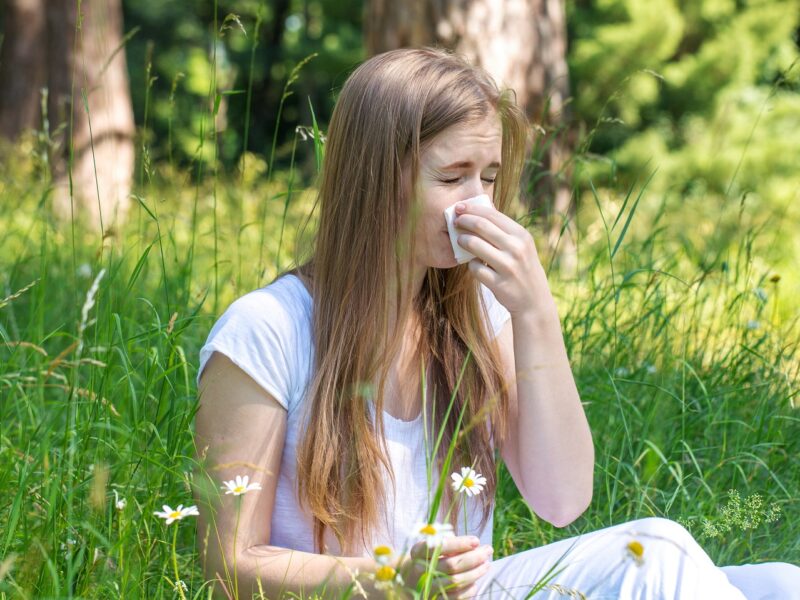 Młoda kobieta siedzi na łące, ma alergię na pyłki traw