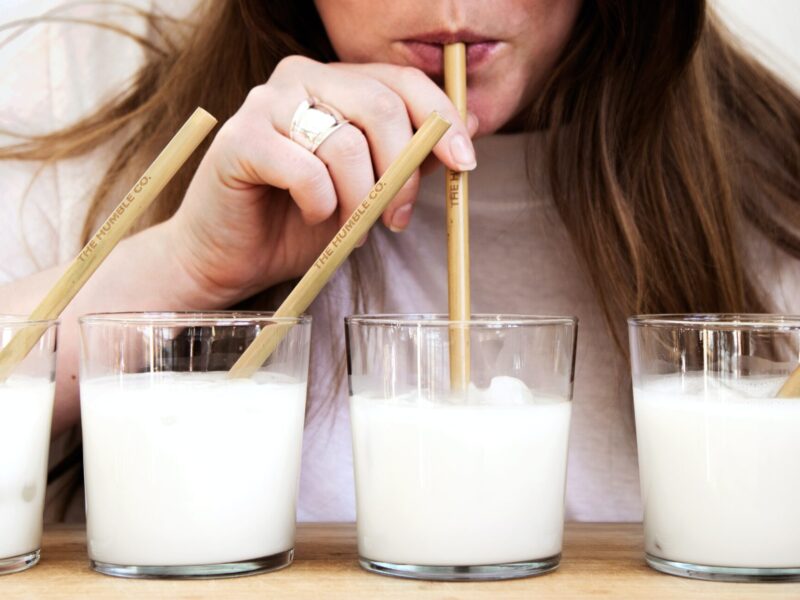 Cztery szklanki mleka ze słomkami, z jednej pije kobieta, alergia na mleko
