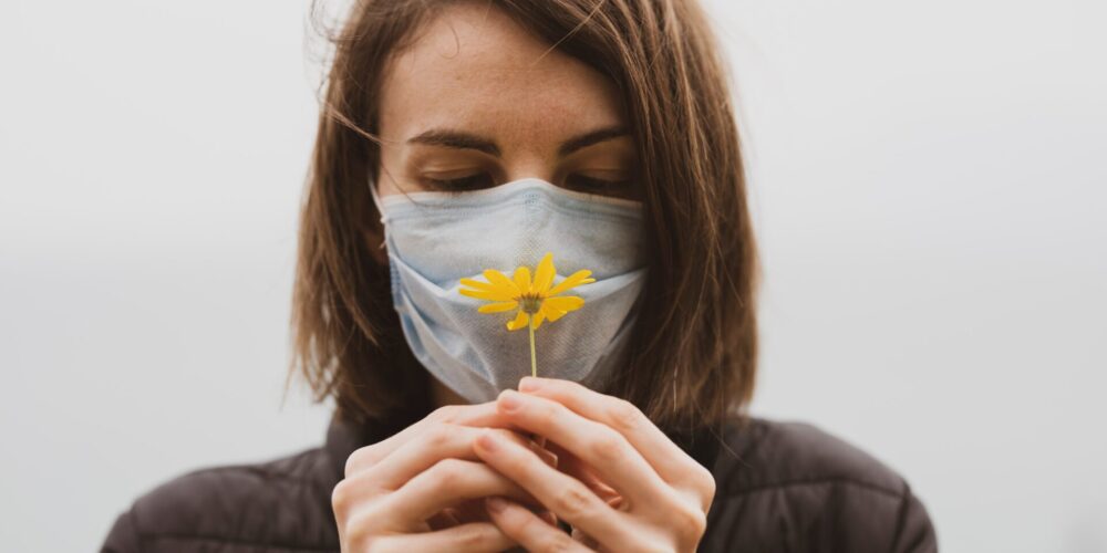 kobieta w maseczce trzyma w ręku żółty kwiatek, diagnozowanie alergii