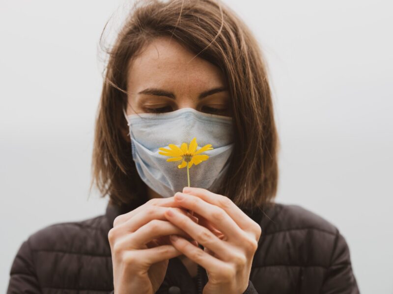 kobieta w maseczce trzyma w ręku żółty kwiatek, diagnozowanie alergii