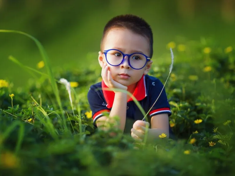chłopiec w okularach siedzi na łące