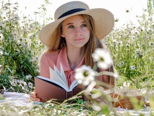 Dziewczyna z kapeluszem czytająca książkę na łące, trawy, pyłki w lipcu