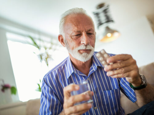Mężczyzna trzyma blister z tabletkami i szklankę wody, alergia na leki